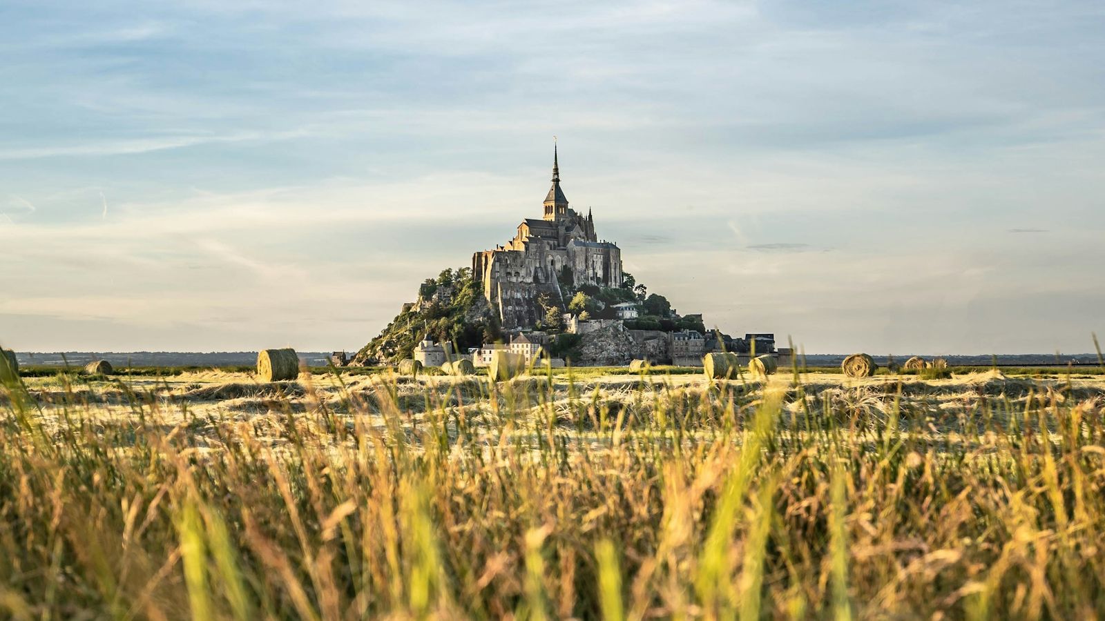 Mont-Saint-Michel and its abbey rising above the fields and bay of Normandy, France, in golden summer light
