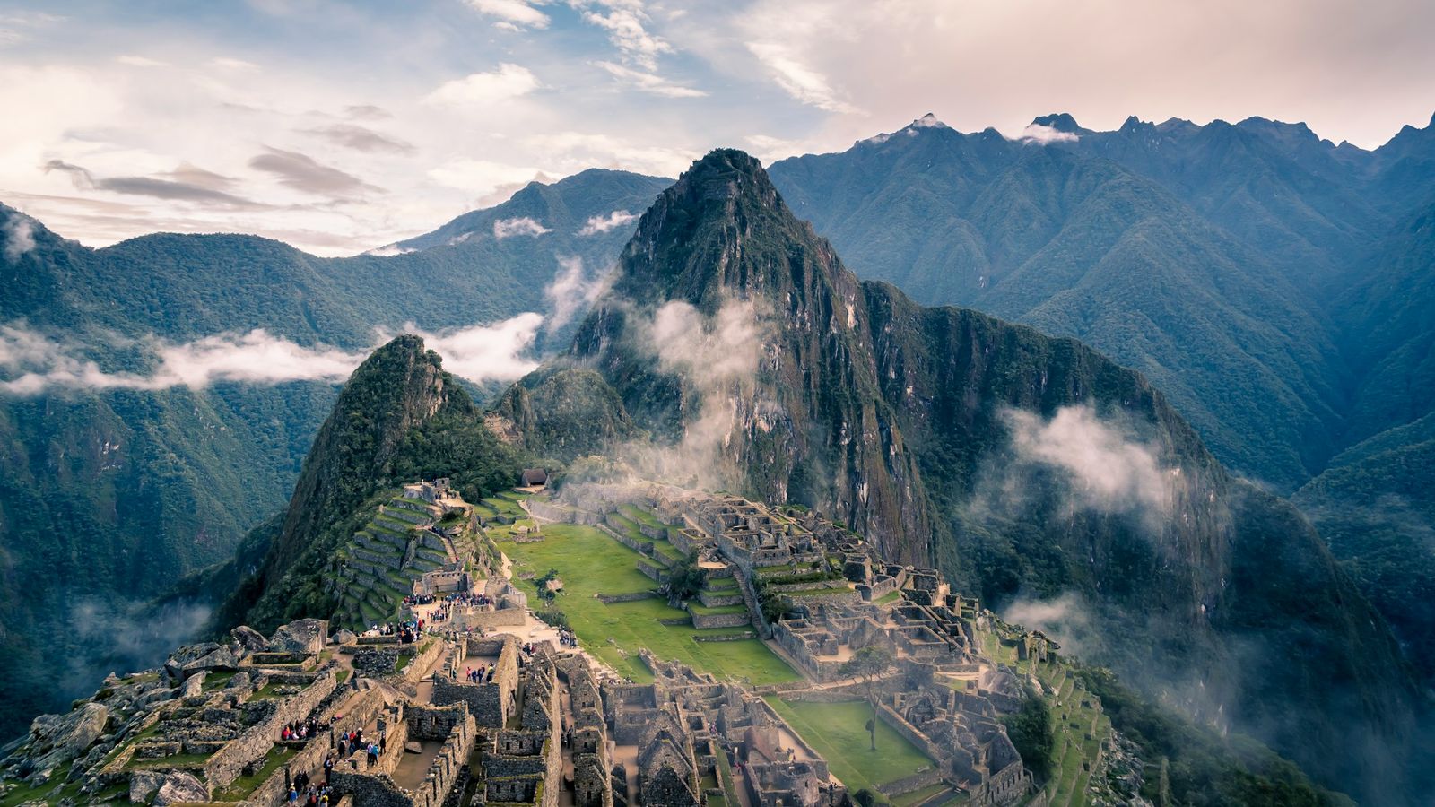 The terraces and stone buildings of Machu Picchu on a ridge above the Urubamba valley, Peru, with mountains and mist behind