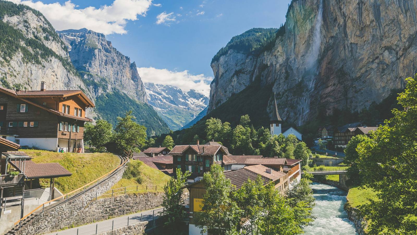 Wooden chalets in the Lauterbrunnen valley, Switzerland, with a waterfall dropping from the cliffs and Alpine peaks behind
