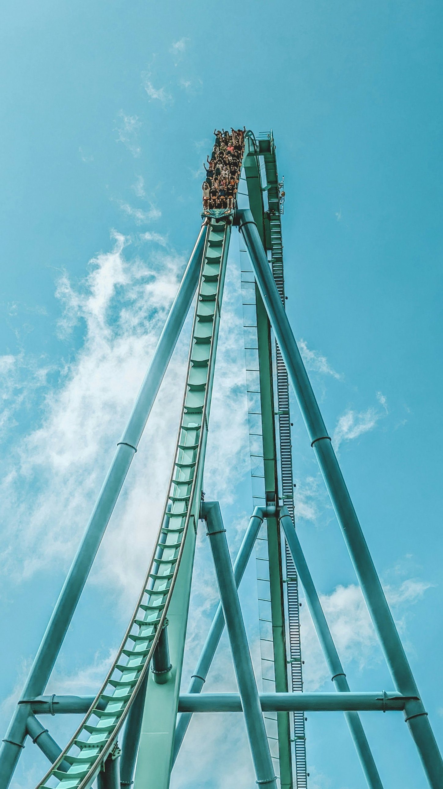 A roller coaster train cresting the top of a tall green lift hill against a blue sky
